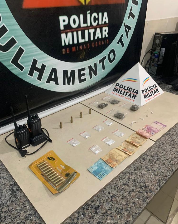 armas e drogas em live
Foto oficial dos materias apreendidos listados em texto corrido, dispostos sobre uma mesa de granito com uma placa de madeira clara por cima, frnete ao banner na polícia militar de Viçosa.