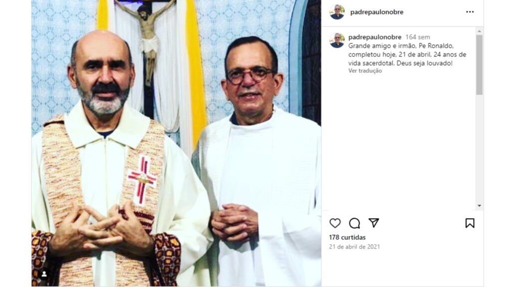 Texto alternativo: Padre Paulo Nobre, à direita, e Padre Ronaldo, à esquerda, ambos com vestes religiosas e mãos unidas à frente, em gesto de oração e reverência.
