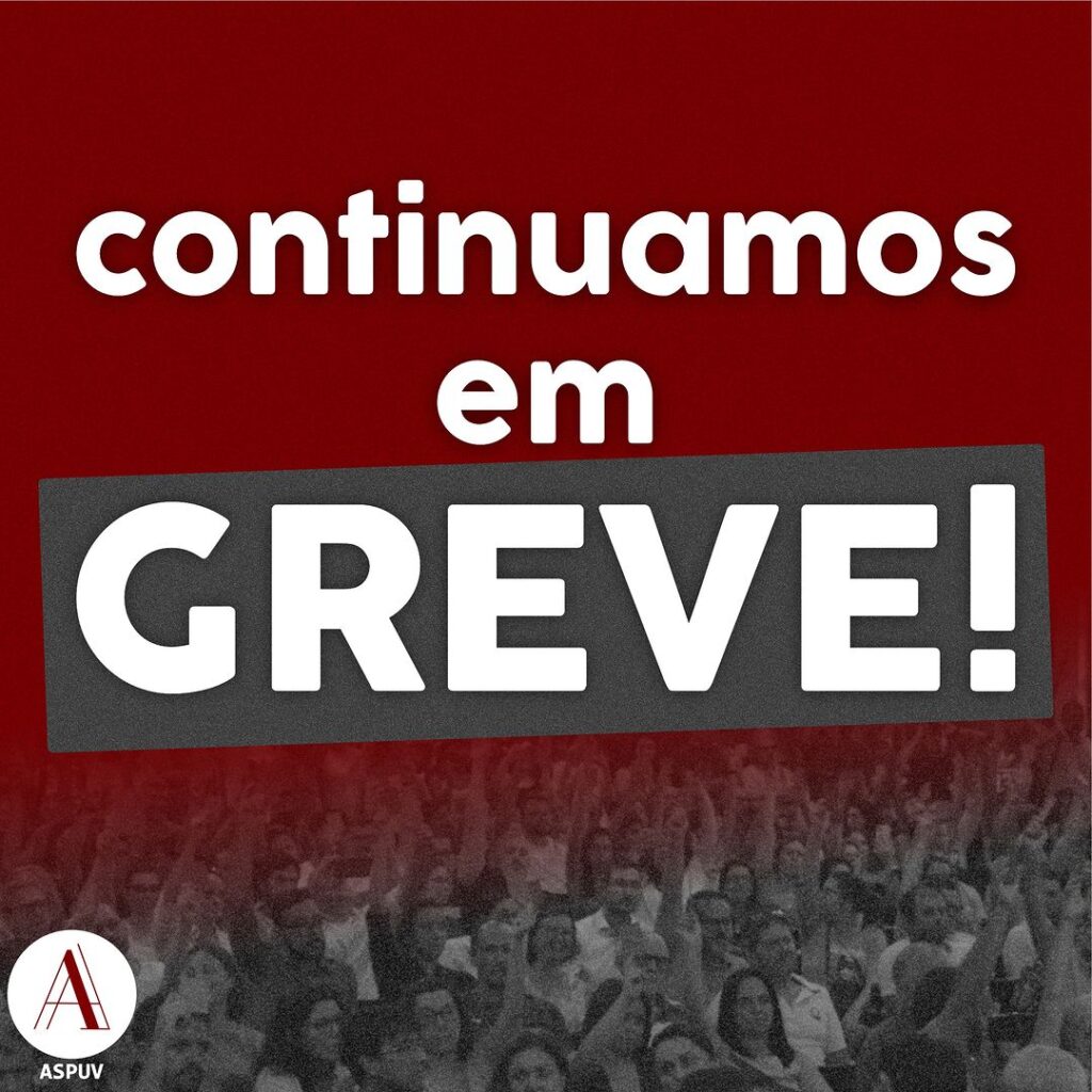 Arte do Instagram da "ASPUV" com o texto "Continuamos em Greve!" em caixa alto, num tamanho grande e em destaque frente a um fundo metade vermelho, metade foto em preto e branco de professores com mão levantandas.